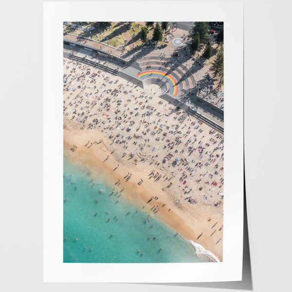 Aerial view of a beach with people and a rainbow, framed against a white background.